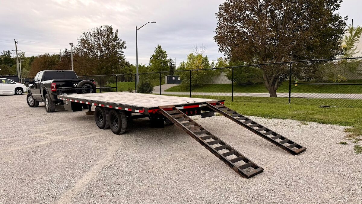 8x20 equipment deckover trailer hitched and loaded with the slide-out ramps set, for rent in York Region